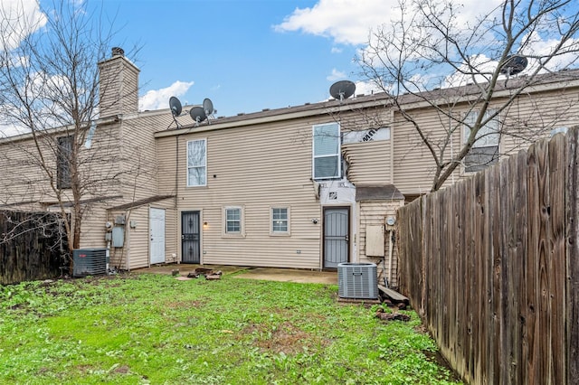 rear view of house featuring a patio area, central AC, fence, and a lawn