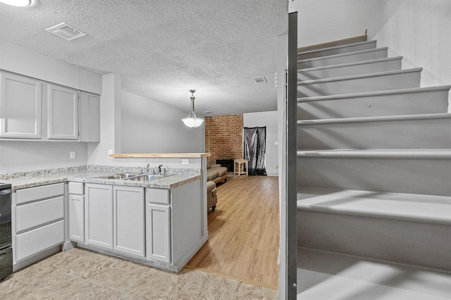 kitchen featuring visible vents, a brick fireplace, a sink, a textured ceiling, and a peninsula