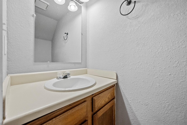 bathroom featuring a textured ceiling, a textured wall, and vanity