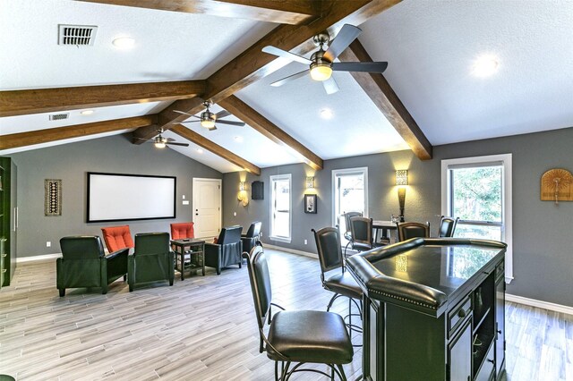 living room with lofted ceiling with beams, light wood finished floors, and visible vents