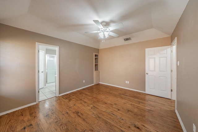 spare room featuring ceiling fan, wood finished floors, visible vents, baseboards, and vaulted ceiling