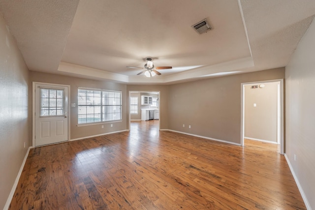 empty room with hardwood / wood-style floors, a tray ceiling, visible vents, and baseboards