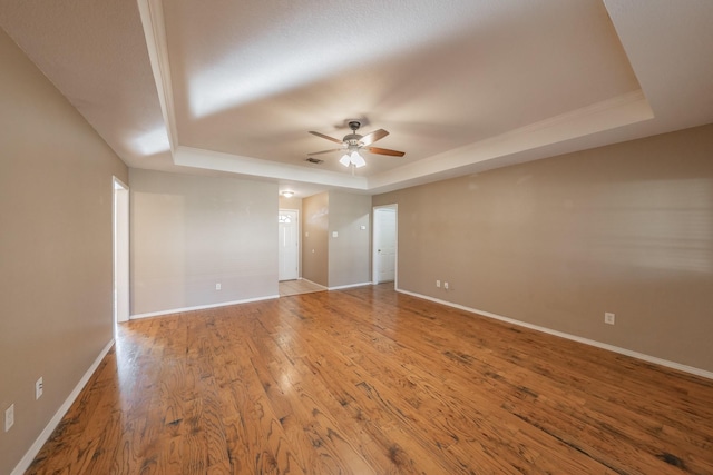 empty room featuring visible vents, baseboards, a raised ceiling, a ceiling fan, and wood-type flooring