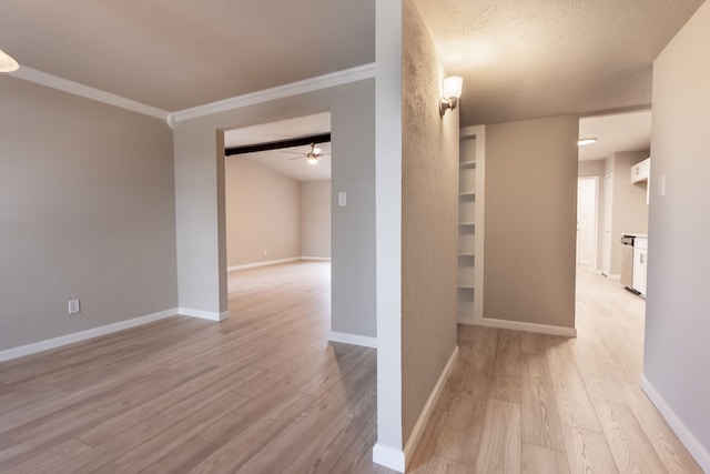 hallway with a textured ceiling, ornamental molding, light wood-style flooring, and baseboards