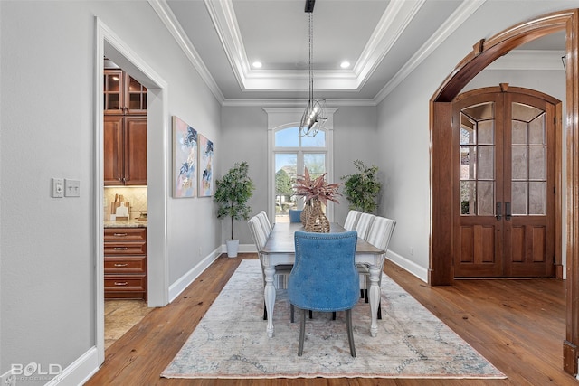 dining area with arched walkways, french doors, crown molding, a raised ceiling, and hardwood / wood-style floors