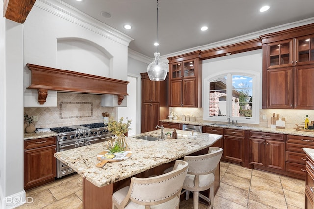 kitchen with crown molding, a center island with sink, appliances with stainless steel finishes, a sink, and light stone countertops