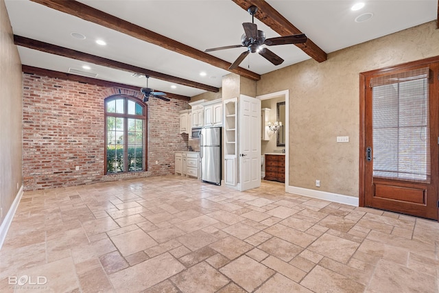 unfurnished living room with beamed ceiling, stone tile flooring, a ceiling fan, and baseboards