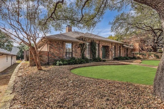 view of front facade with a front yard, a chimney, and brick siding