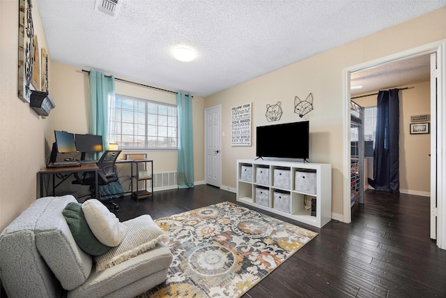 living room featuring wood-type flooring, visible vents, a textured ceiling, and baseboards