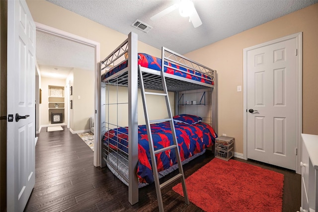 bedroom featuring a textured ceiling, hardwood / wood-style flooring, visible vents, baseboards, and a ceiling fan