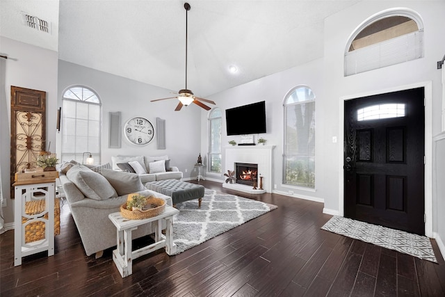 living area featuring dark wood-style floors, visible vents, ceiling fan, a lit fireplace, and baseboards