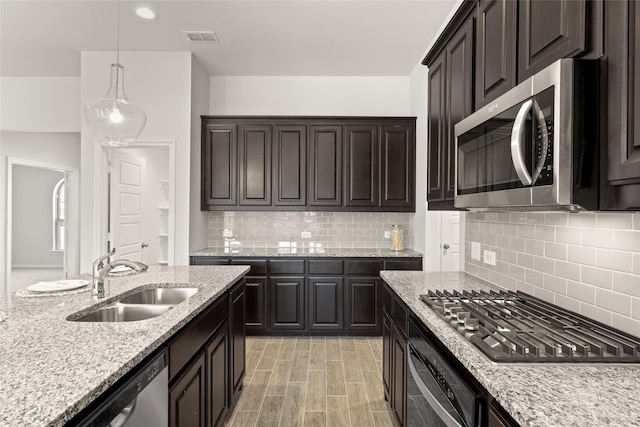 kitchen featuring light stone counters, visible vents, a sink, hanging light fixtures, and stainless steel appliances