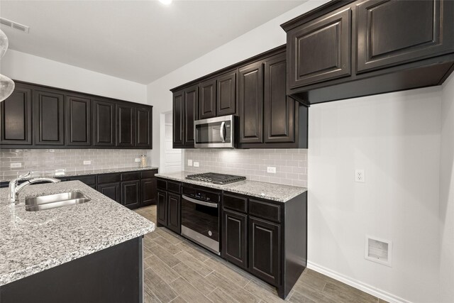 kitchen with light stone countertops, visible vents, wood tiled floor, a sink, and stainless steel appliances