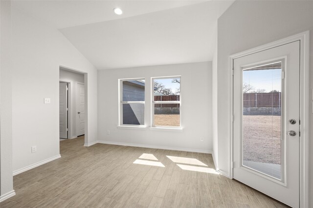 spare room with lofted ceiling, light wood-style flooring, and baseboards