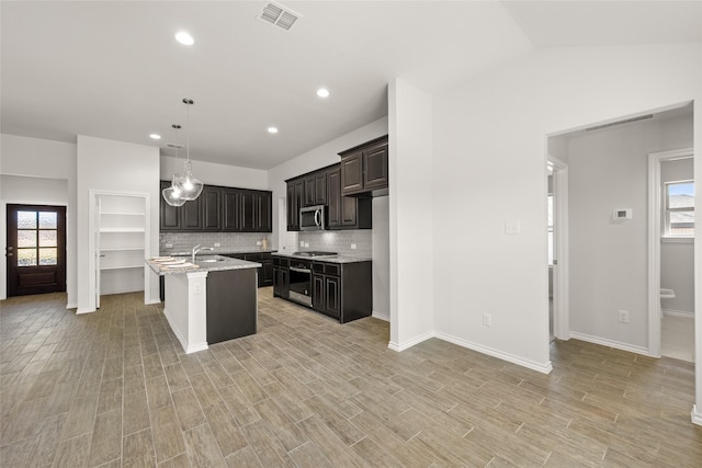 kitchen featuring visible vents, light wood-style flooring, a kitchen island with sink, a sink, and stainless steel appliances