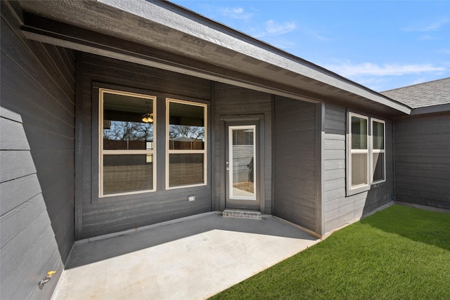 doorway to property featuring a patio area, a lawn, and roof with shingles