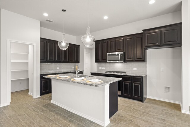 kitchen with wood finish floors, stainless steel appliances, visible vents, and a kitchen island with sink