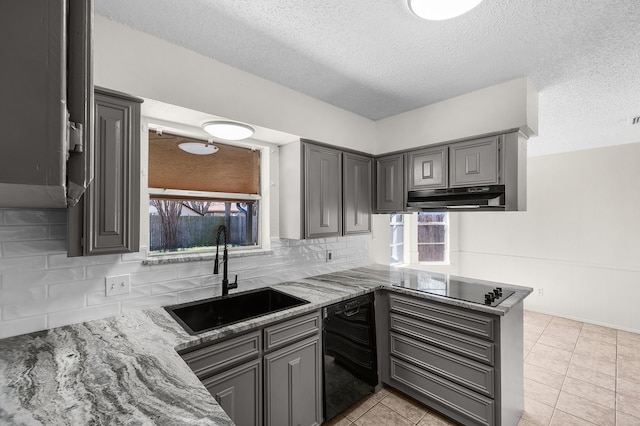 kitchen featuring light stone counters, under cabinet range hood, gray cabinetry, black appliances, and a sink