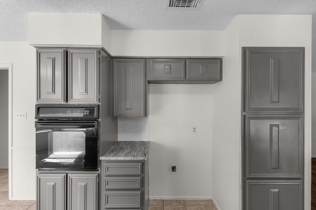 kitchen with light tile patterned floors, backsplash, oven, and gray cabinetry