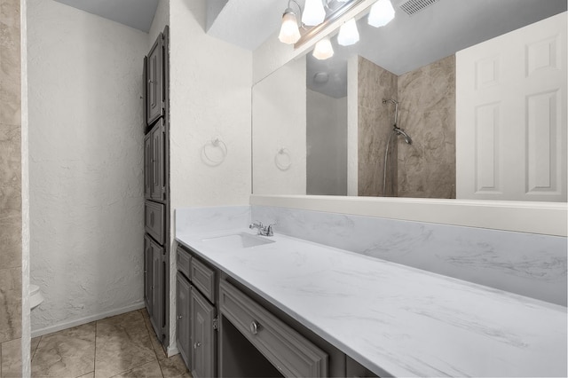 full bathroom with a textured wall, a tile shower, vanity, baseboards, and tile patterned floors