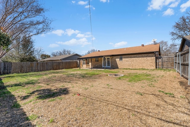 rear view of property with a fire pit, french doors, a fenced backyard, a yard, and brick siding