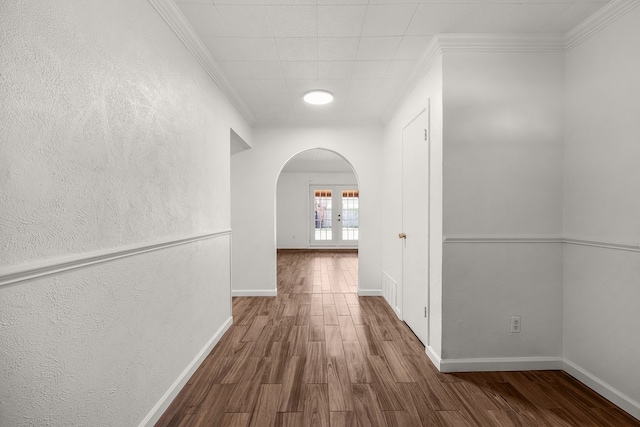 hall featuring arched walkways, crown molding, baseboards, and wood finished floors