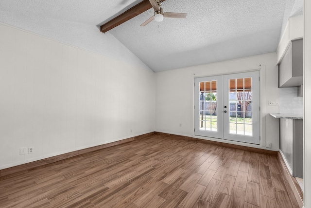 unfurnished living room with vaulted ceiling with beams, ceiling fan, a textured ceiling, wood finished floors, and french doors