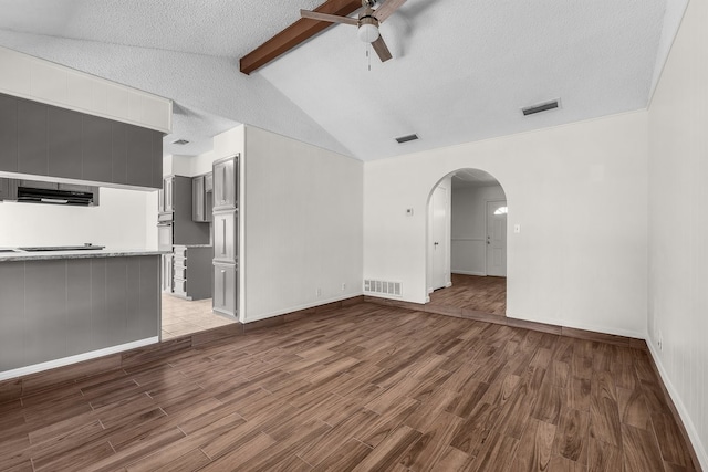 unfurnished living room with arched walkways, visible vents, vaulted ceiling with beams, and wood finished floors