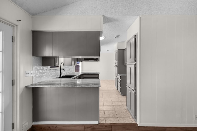 kitchen featuring light tile patterned floors, visible vents, light stone counters, a peninsula, and a sink