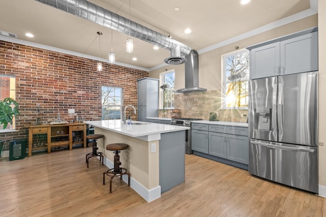 kitchen with light wood-style flooring, gray cabinetry, stainless steel appliances, ornamental molding, and wall chimney exhaust hood