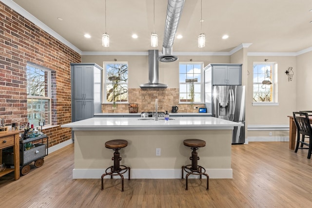 kitchen with wall chimney exhaust hood, a breakfast bar, stainless steel refrigerator with ice dispenser, and brick wall