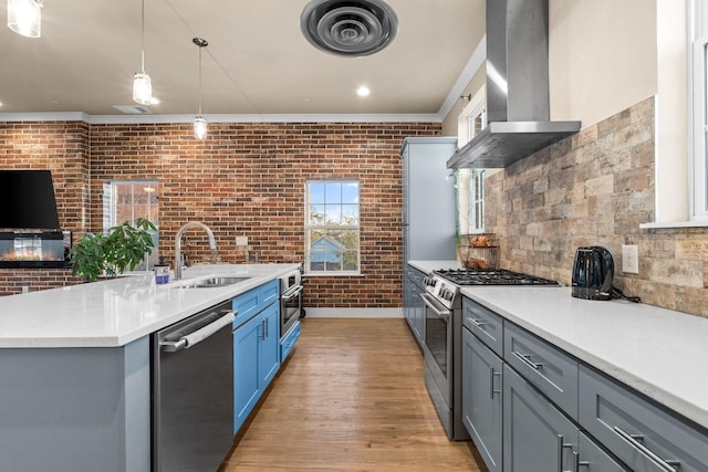 kitchen featuring brick wall, a sink, visible vents, wall chimney range hood, and appliances with stainless steel finishes