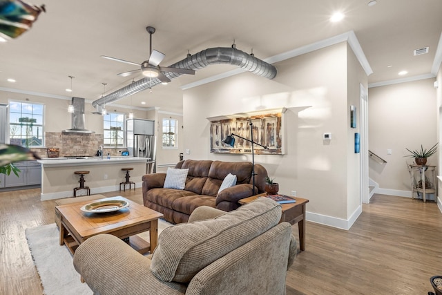 living room featuring ornamental molding, light wood-style floors, visible vents, and a healthy amount of sunlight