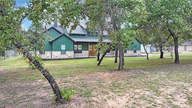 exterior space featuring stone siding, roof with shingles, and a front lawn