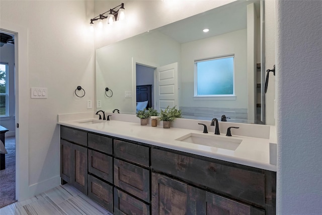 full bath featuring baseboards, double vanity, a sink, and connected bathroom