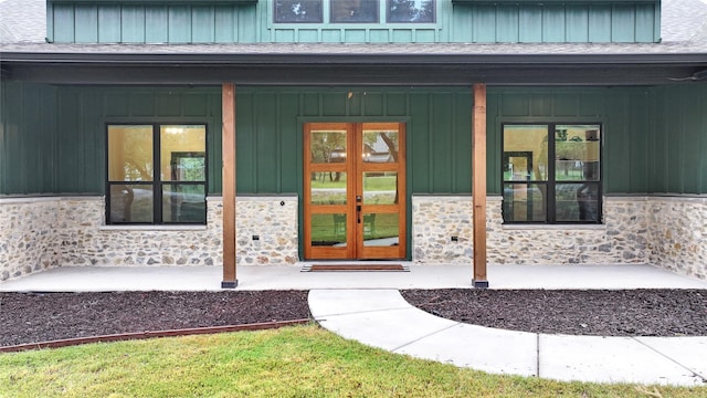 entrance to property featuring board and batten siding, stone siding, roof with shingles, and french doors