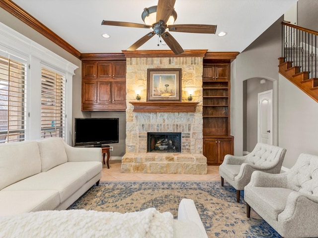 living room with arched walkways, crown molding, light tile patterned floors, a ceiling fan, and a stone fireplace