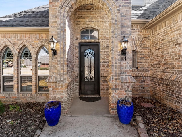 doorway to property with roof with shingles and brick siding