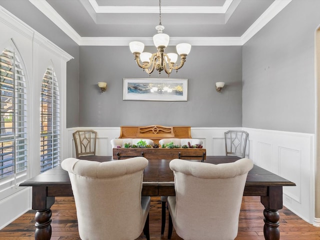 dining space with an inviting chandelier, wood-type flooring, a raised ceiling, and wainscoting