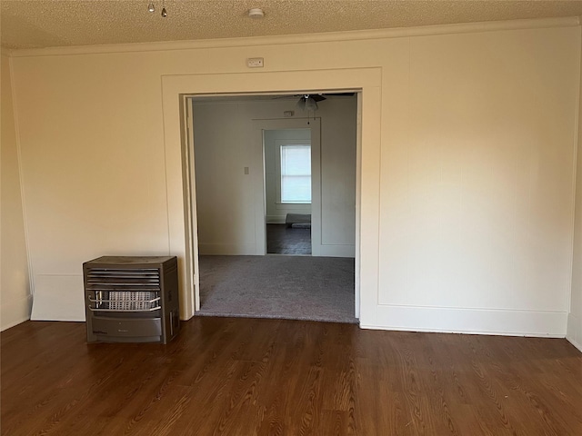 empty room featuring dark wood-type flooring, ornamental molding, a textured ceiling, and heating unit