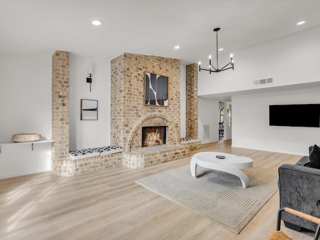 living room with a notable chandelier, recessed lighting, visible vents, a brick fireplace, and wood finished floors