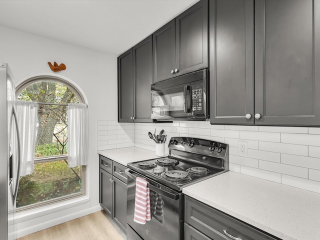 kitchen featuring baseboards, black appliances, light wood-style flooring, and decorative backsplash