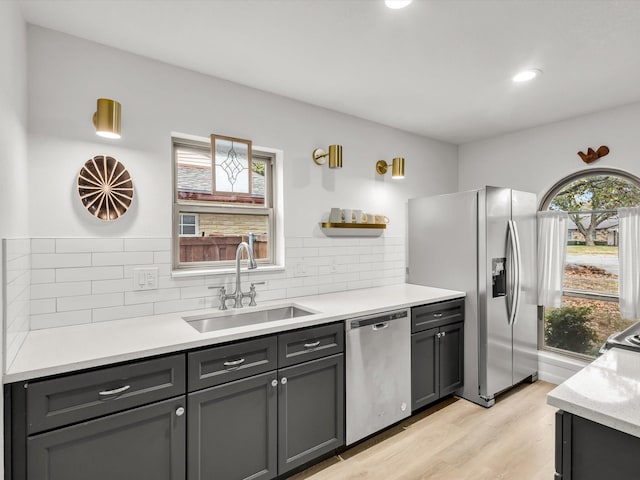 kitchen featuring appliances with stainless steel finishes, a sink, light countertops, light wood-type flooring, and backsplash