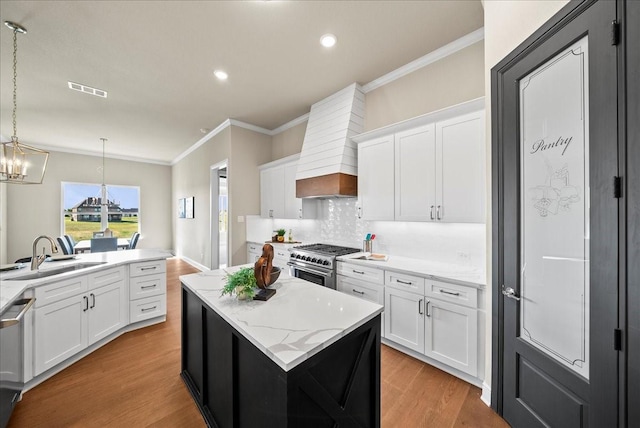 kitchen with a kitchen island, ornamental molding, a sink, appliances with stainless steel finishes, and light wood-type flooring