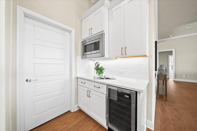 kitchen with stainless steel microwave, beverage cooler, light wood-type flooring, and backsplash