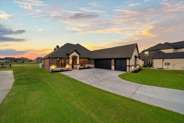 french country home featuring a front yard, an attached garage, concrete driveway, stone siding, and brick siding