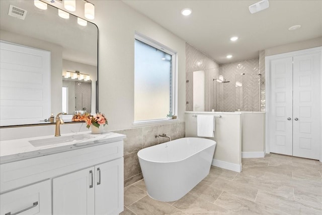 bathroom featuring visible vents, tile walls, a tile shower, a soaking tub, and vanity