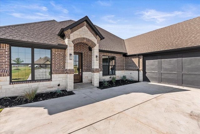 french country home featuring stone siding, roof with shingles, concrete driveway, an attached garage, and brick siding