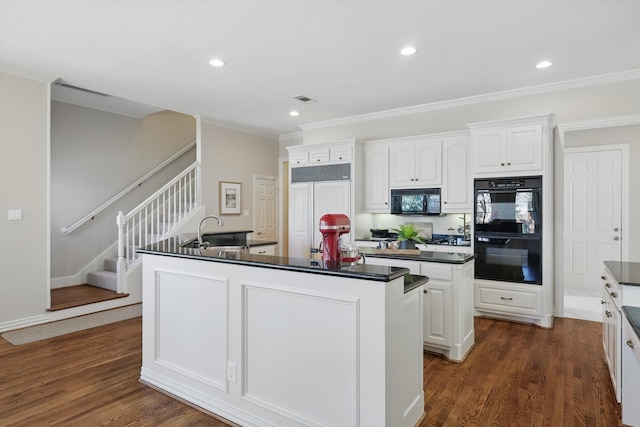 kitchen featuring dark wood-type flooring, a sink, black appliances, dark countertops, and a center island with sink