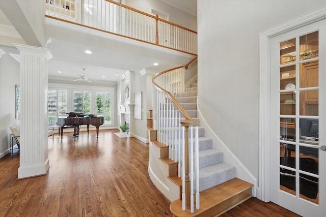 stairway with a high ceiling, wood finished floors, a ceiling fan, baseboards, and decorative columns